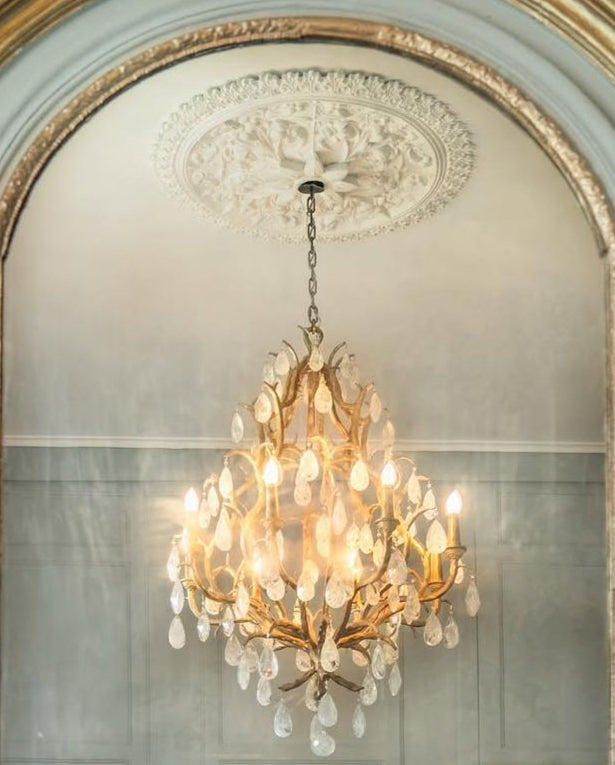 Decorative mirror with gold frame and chandelier reflection on a light blue wall.